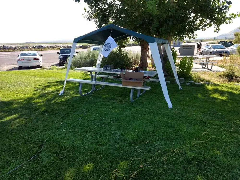 A portable radio station on a picnic table under a canopy, set up for a Parks on the Air activation