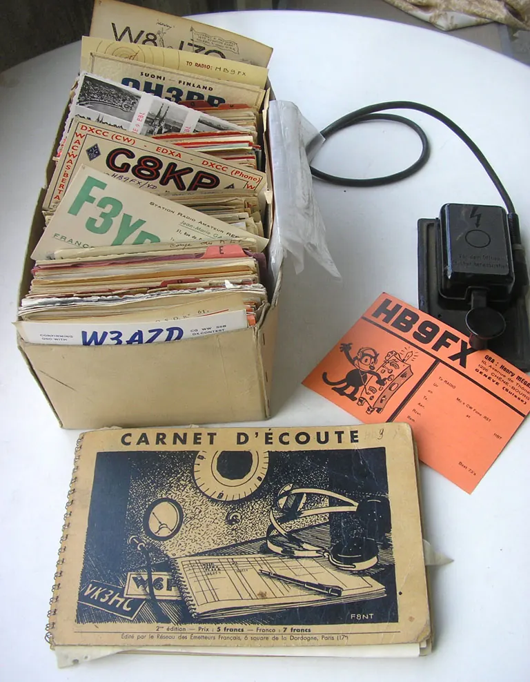 A box of QSL cards from 1946 to 1969 beside a listening log and a Morse key