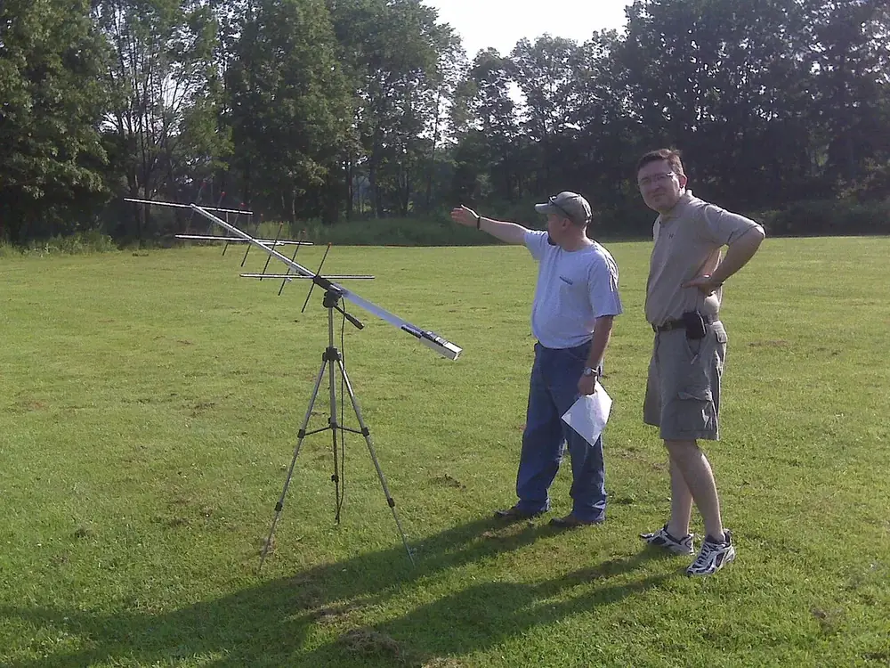 Two operators beside a Yagi antenna on a tripod, watching the horizon for a satellite pass