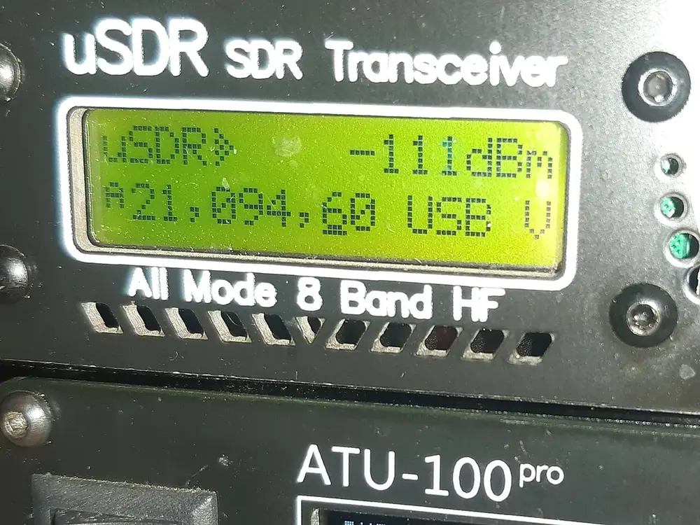 A compact uSDR HF transceiver showing 21.094 MHz on a green LCD, above an ATU-100 antenna tuner